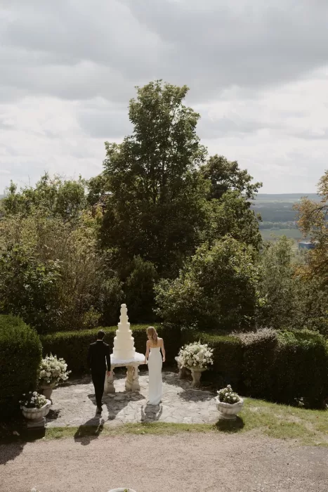 Bride and groom approaching a towering wedding cake on a garden terrace at Château du Prieuré d’Evecquemont.