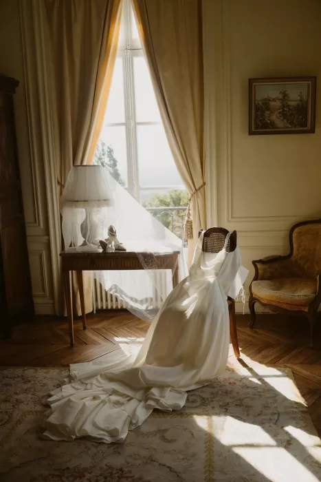 Bridal dress and veil styled by a window inside Château du Prieuré d’Evecquemont, illuminated by soft natural light.