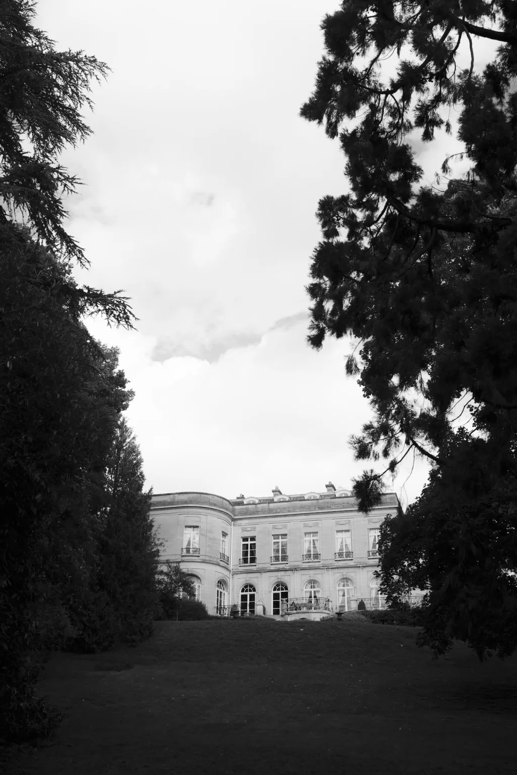 Black and white exterior view of Château du Prieuré d’Evecquemont framed by trees and landscaped grounds.