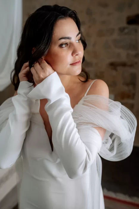 Close-up portrait of the bride at Finca Morneta adjusting her earring, wearing a modern white gown with sheer detailing.