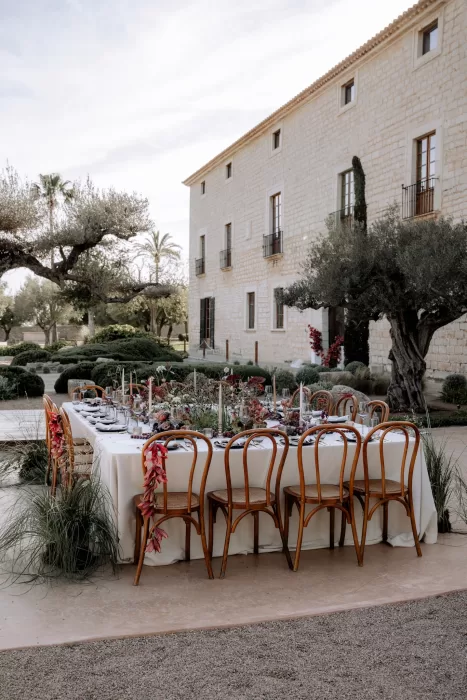 Outdoor reception table at Finca Morneta styled with white linens, wooden chairs and abundant florals in the Mediterranean garden.
