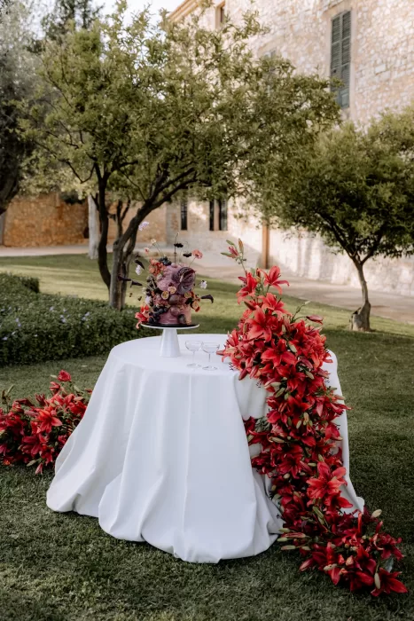 Statement wedding cake displayed in the gardens of Finca Morneta, surrounded by dramatic red florals and citrus trees.