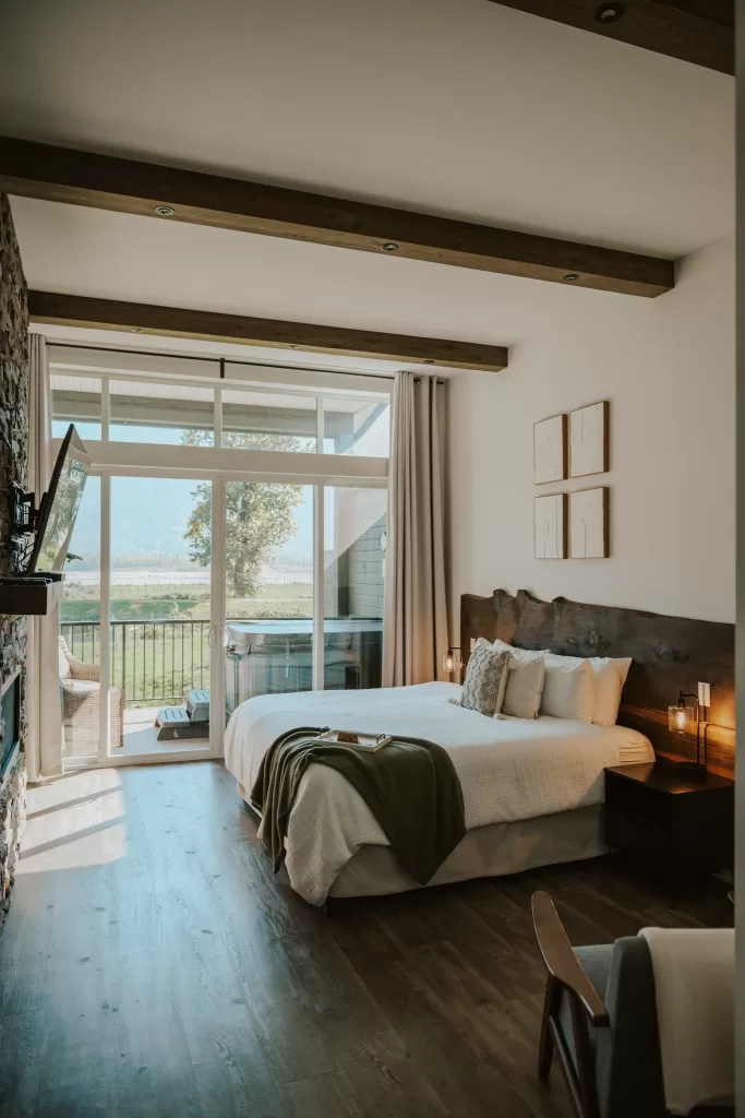 Modern guest bedroom at Fraser River Lodge with balcony doors opening to mountain and river views.