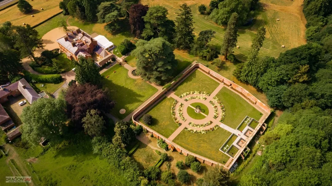 Aerial view of Garthmyl Hall and its formal walled gardens, showcasing manicured lawns, circular pathways and surrounding countryside.