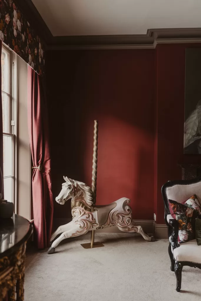 Richly decorated bridal suite at Garthmyl Hall with deep red walls, velvet curtains and a vintage carousel horse adding character to the space.