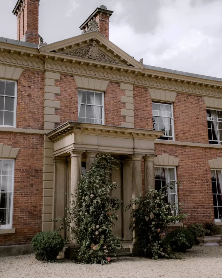 Grand columned entrance of Garthmyl Hall adorned with abundant greenery and floral installations framing the front doorway.