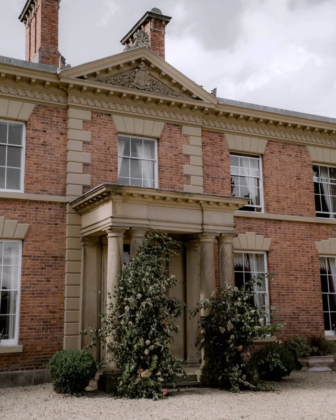 Grand columned entrance of Garthmyl Hall adorned with abundant greenery and floral installations framing the front doorway.