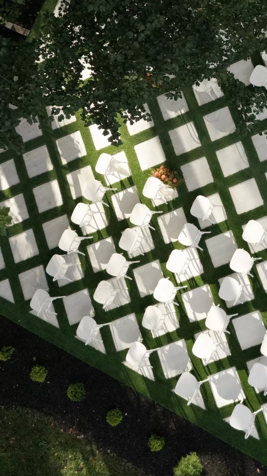 Aerial view of the outdoor ceremony layout at The Greenhouse at Arrows Farm, with white chairs arranged on a geometric lawn beneath trees.