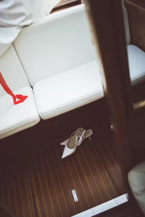 White bridal heels resting on wooden boat floor with red ribbon trailing across seat at Hotel Ristorante La Darsena.