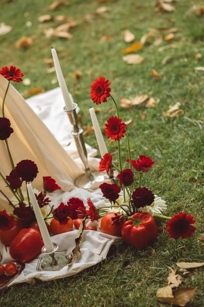 Red floral arrangement with candles, tomatoes and draped fabric set on lawn overlooking Lake Como at Hotel Ristorante La Darsena.