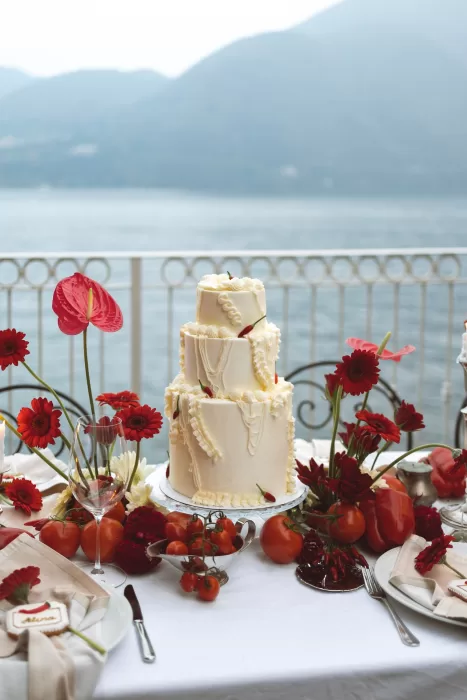 Tiered wedding cake framed by red anthuriums and tomatoes on lakeside terrace at Hotel Ristorante La Darsena.
