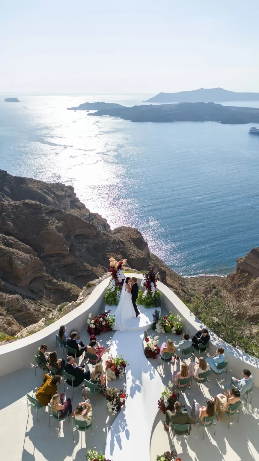 Aerial view of a cliffside wedding ceremony at Islet Santorini, with guests seated around a sculptural aisle above the caldera.