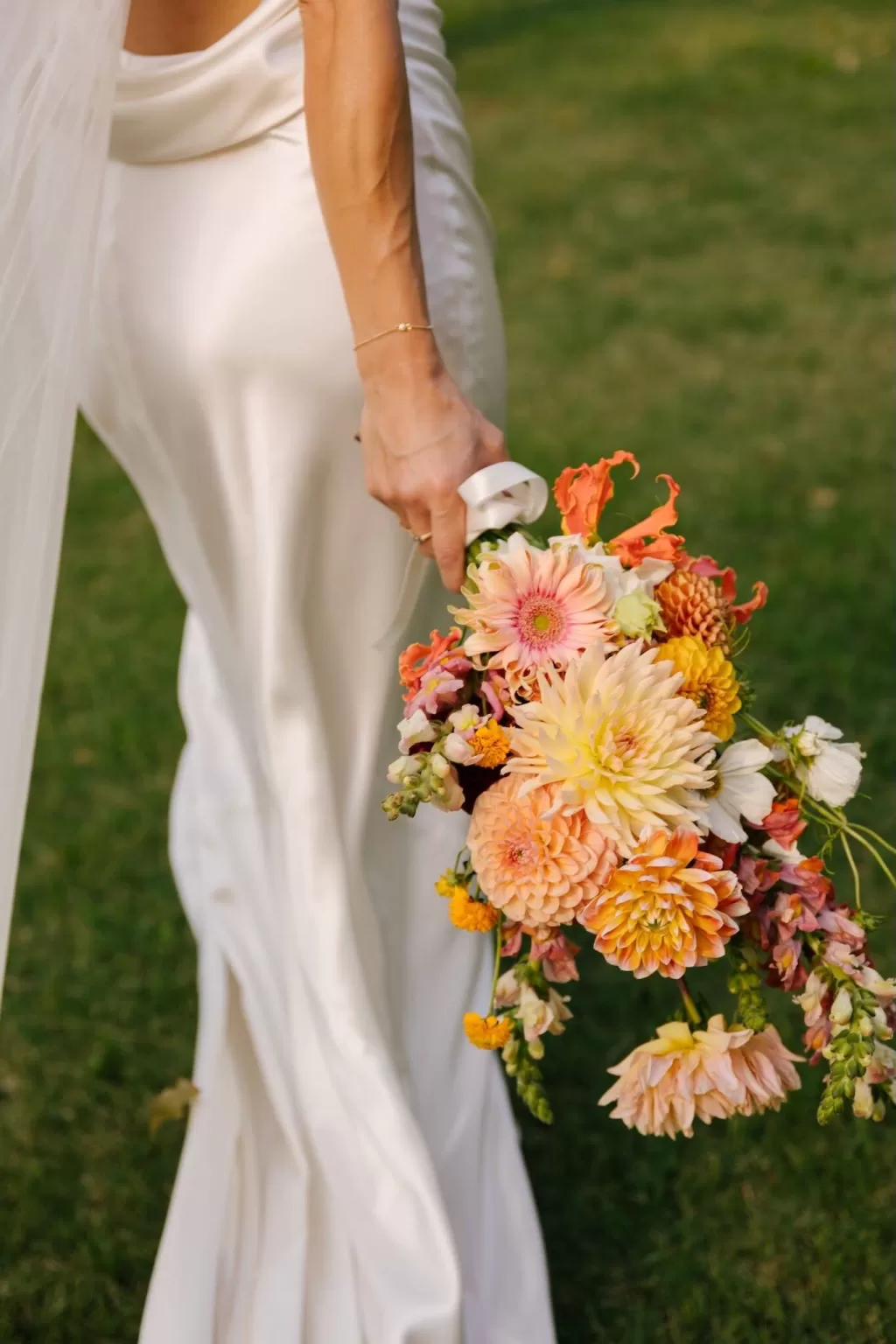 Close-up of the bride holding a vibrant bouquet of dahlias and summer blooms at La Farinera de Sant Lluis.