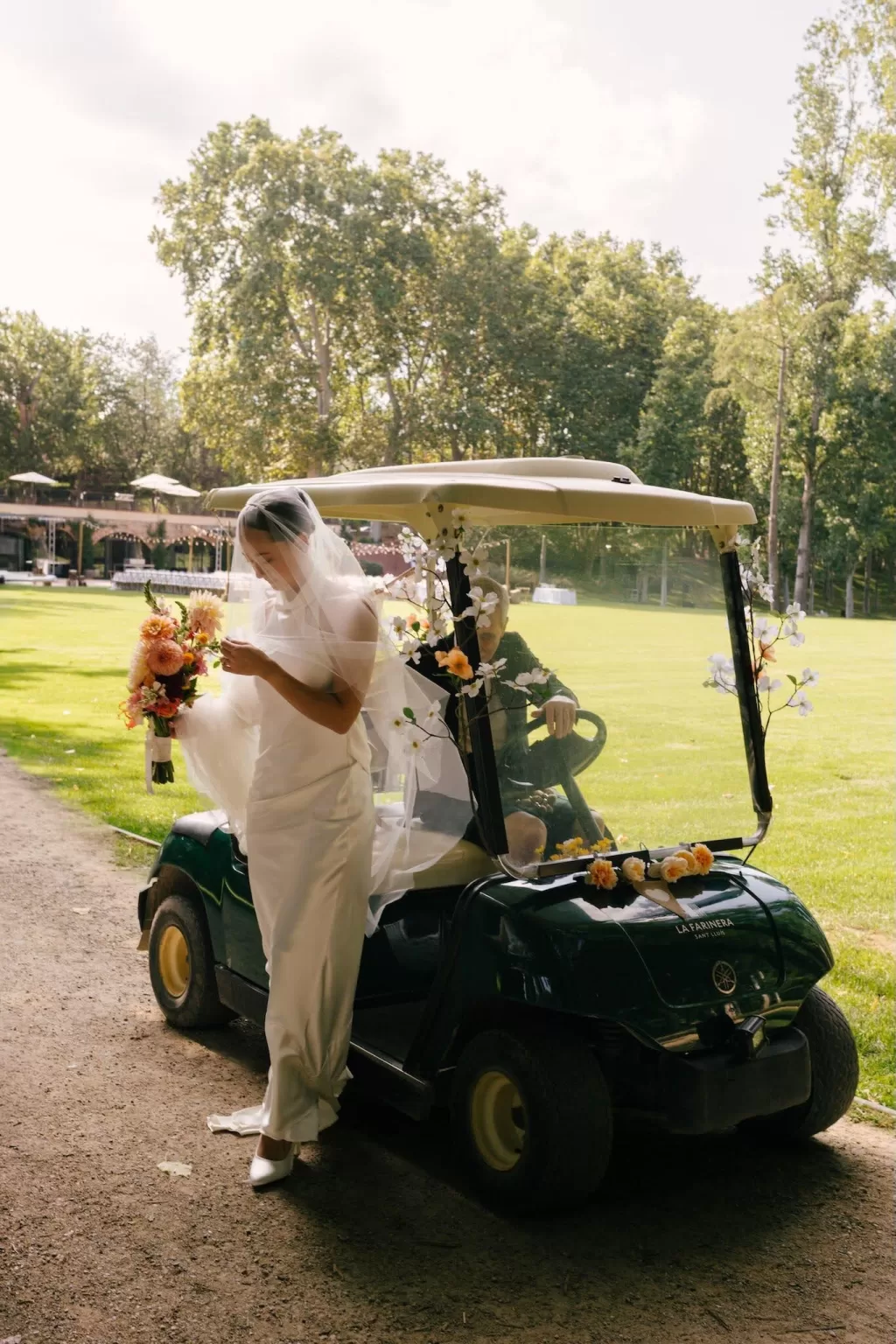 Bride stepping from a decorated golf cart with her bouquet at La Farinera de Sant Lluis.