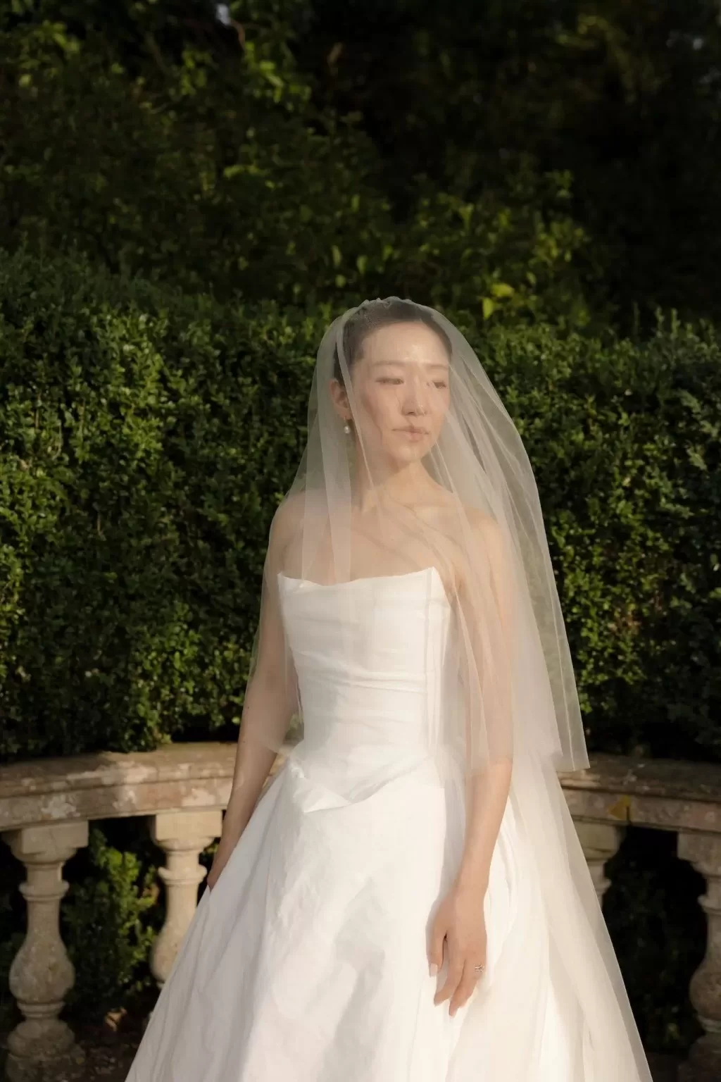 The bride stands in golden sunlight at Manor House, her veil softly framing her serene expression.