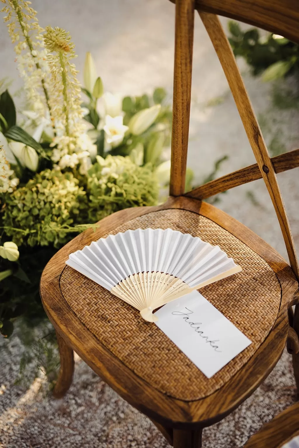 Ceremony chair at Meneghetti Wine Hotel with paper fan and guest name card, surrounded by soft greenery.