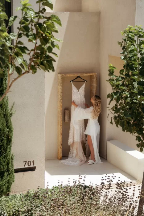 Bride adjusting her wedding dress in private villa suite courtyard at Milos Cove.
