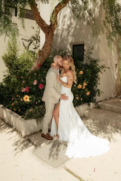 Bride and groom embracing in sunlit Mediterranean garden courtyard at Milos Cove.
