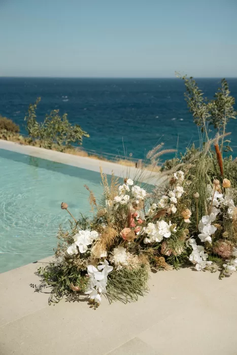 Organic floral arrangement beside infinity pool at Milos Cove overlooking the deep blue Aegean Sea.