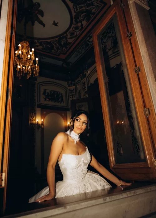 Bride standing by a window at Palacio Metropolitano, her veil softly diffusing natural light over an embroidered satin gown.