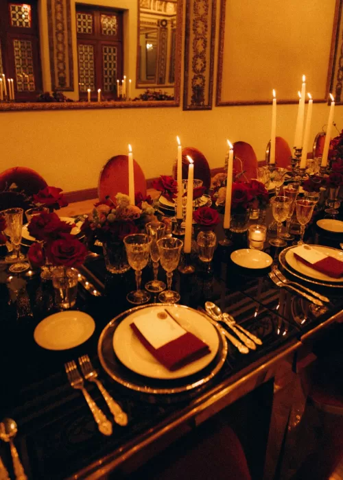 Long banquet table at Palacio Metropolitano styled with tall white candles, red roses and gold-accented tableware.