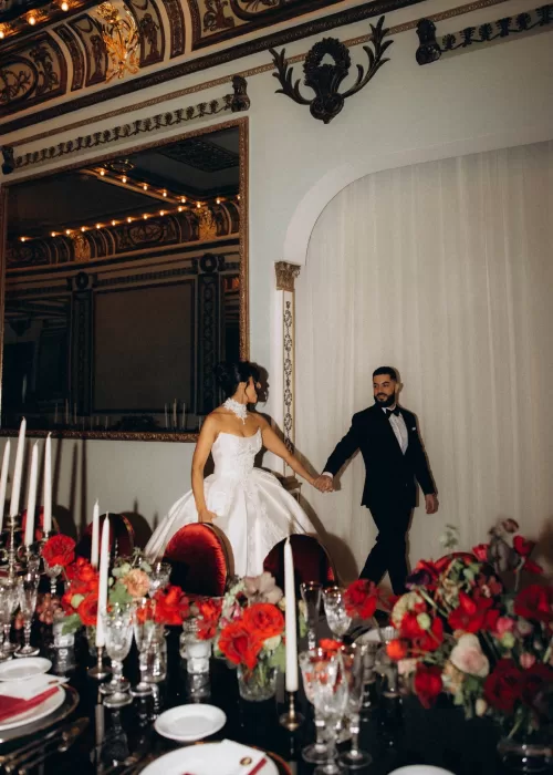 Bride and groom entering the reception at Palacio Metropolitano holding hands beside a candlelit table styled with red roses.
