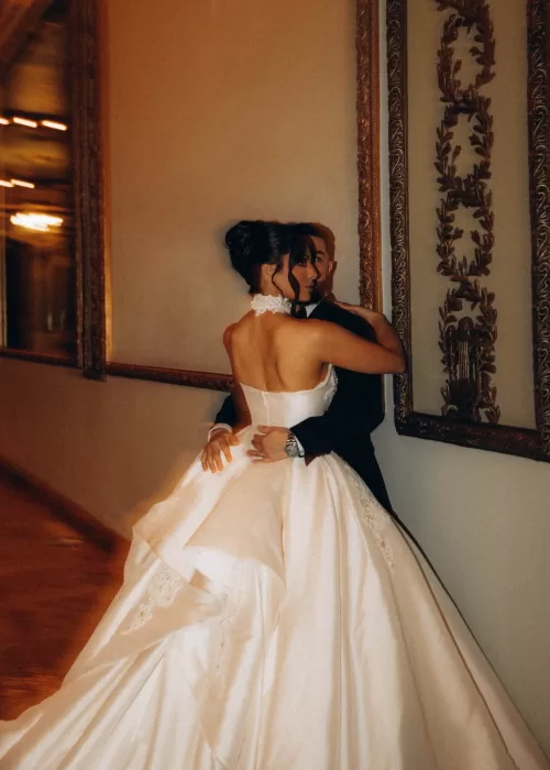 Bride and groom embracing against gilded wall panels inside Palacio Metropolitano, her satin gown cascading dramatically.