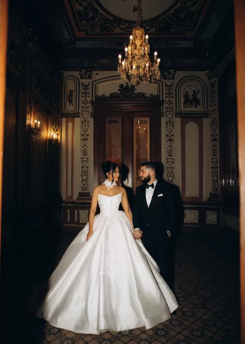 Bride and groom holding hands beneath a crystal chandelier in an opulent corridor at Palacio Metropolitano.