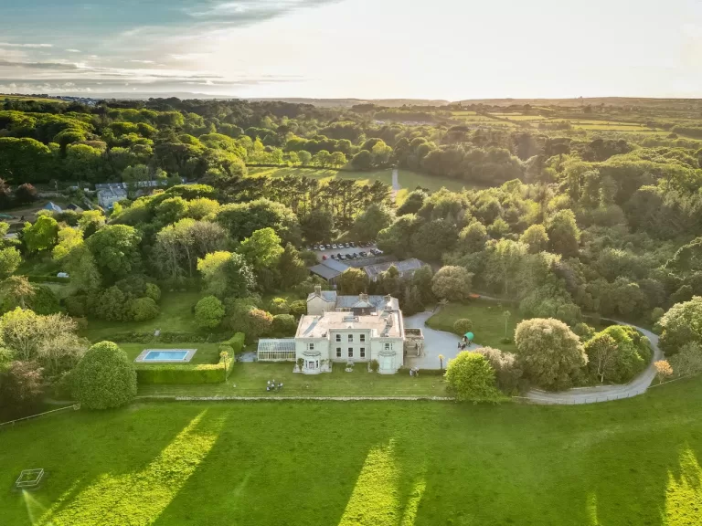 Aerial view of Scorrier House surrounded by rolling countryside, woodland and landscaped gardens at golden hour.