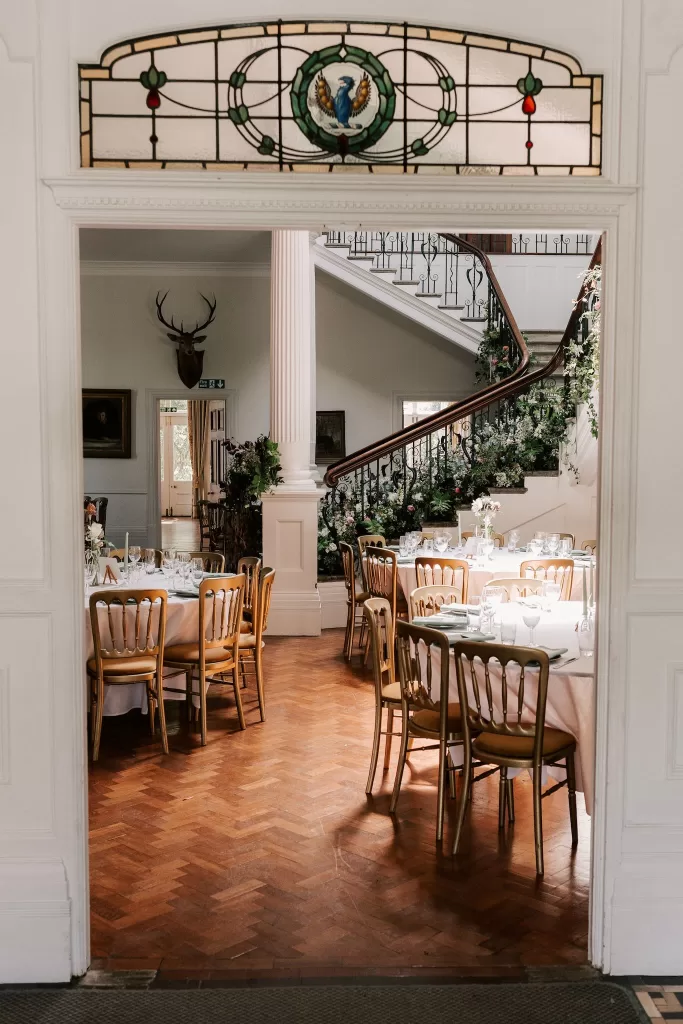 View through an archway into the Scorrier House dining room, with round tables set beneath the grand staircase and classical details.