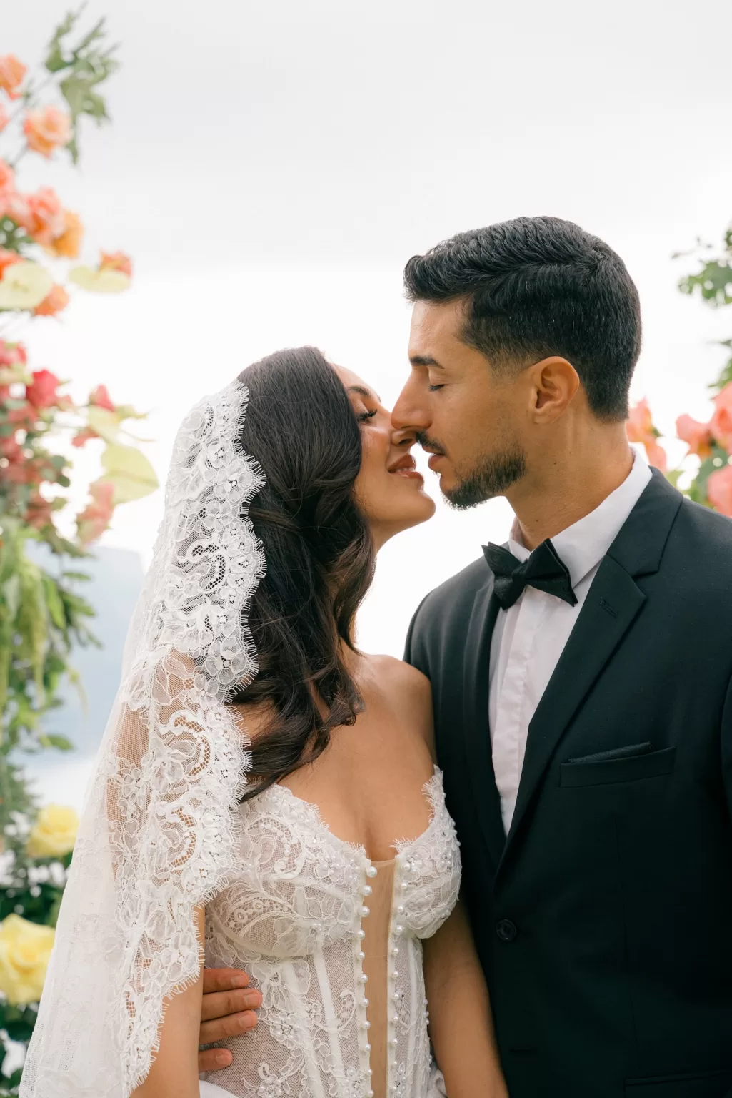 Romantic bride and groom about to kiss beneath abundant peach florals, captured by Sim Sawyers Photography