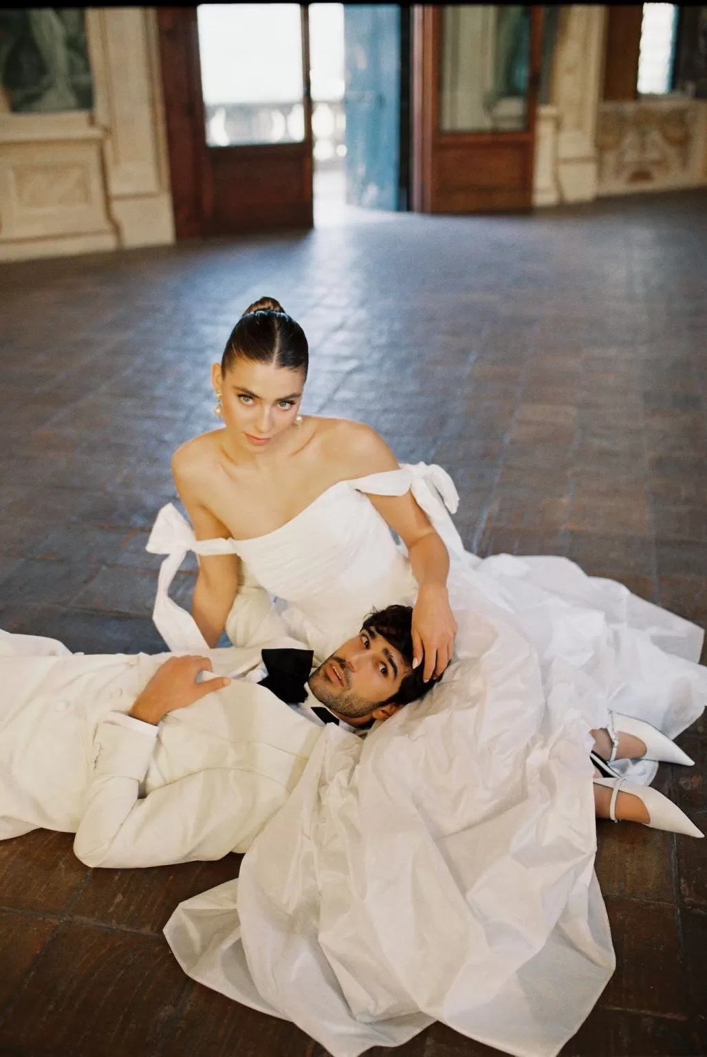 Bride and groom in white attire seated on the floor of Villa Arvedi’s grand hall.