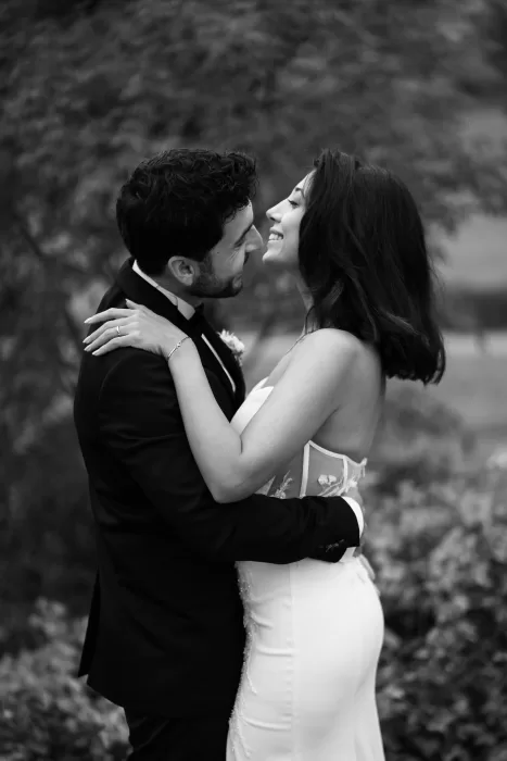 Black and white portrait of bride and groom embracing in the gardens of Villa Honegg surrounded by autumn foliage.