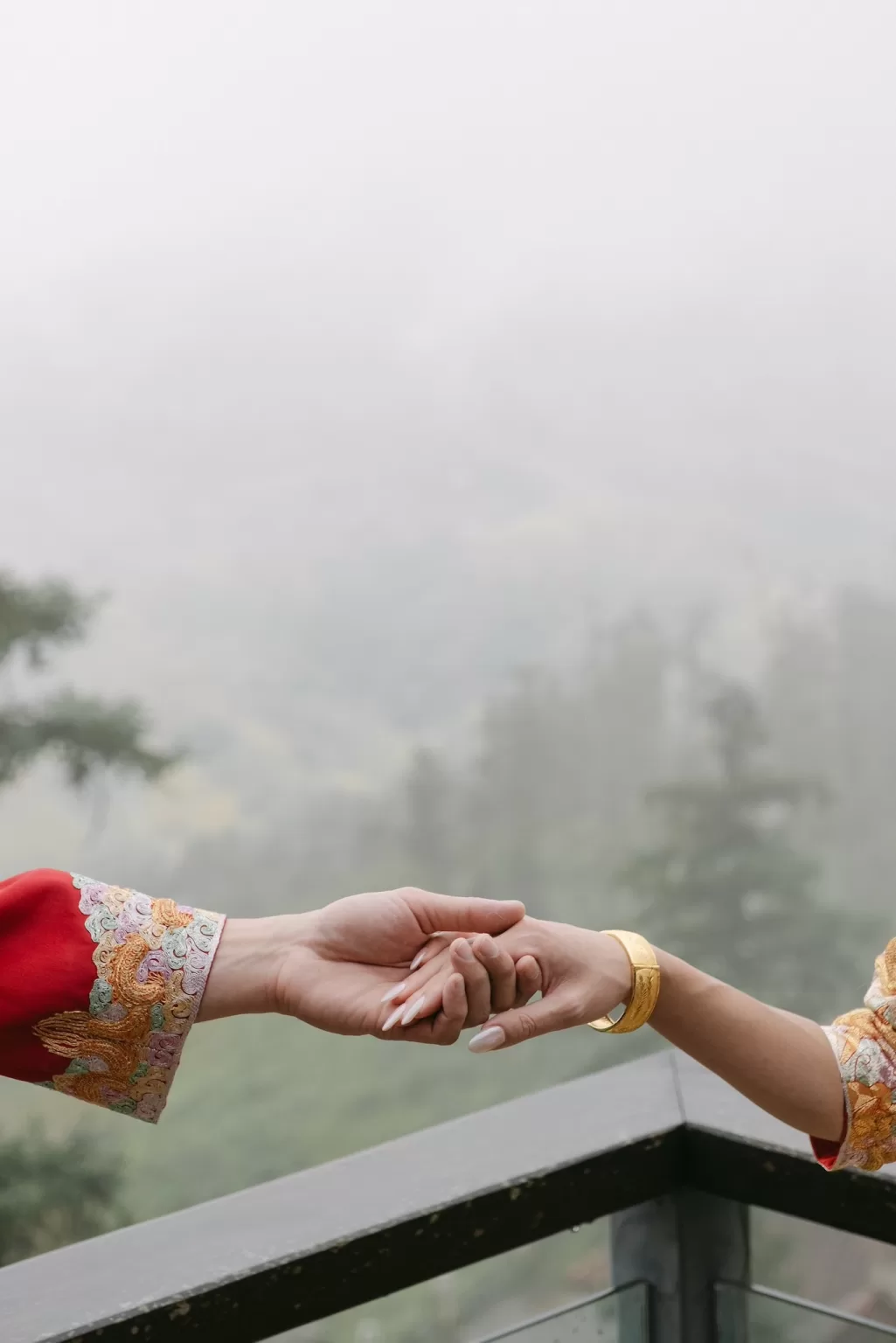 Close-up of the couple holding hands on a balcony at Ville de Mont Mountain Resort with misty mountains fading into the background.