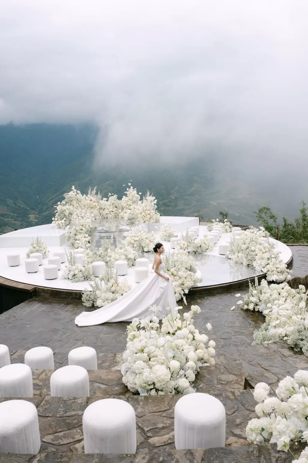 Bride in a strapless gown standing gracefully on a white floral ceremony platform with dramatic mountain views at Ville de Mont Mountain Resort.