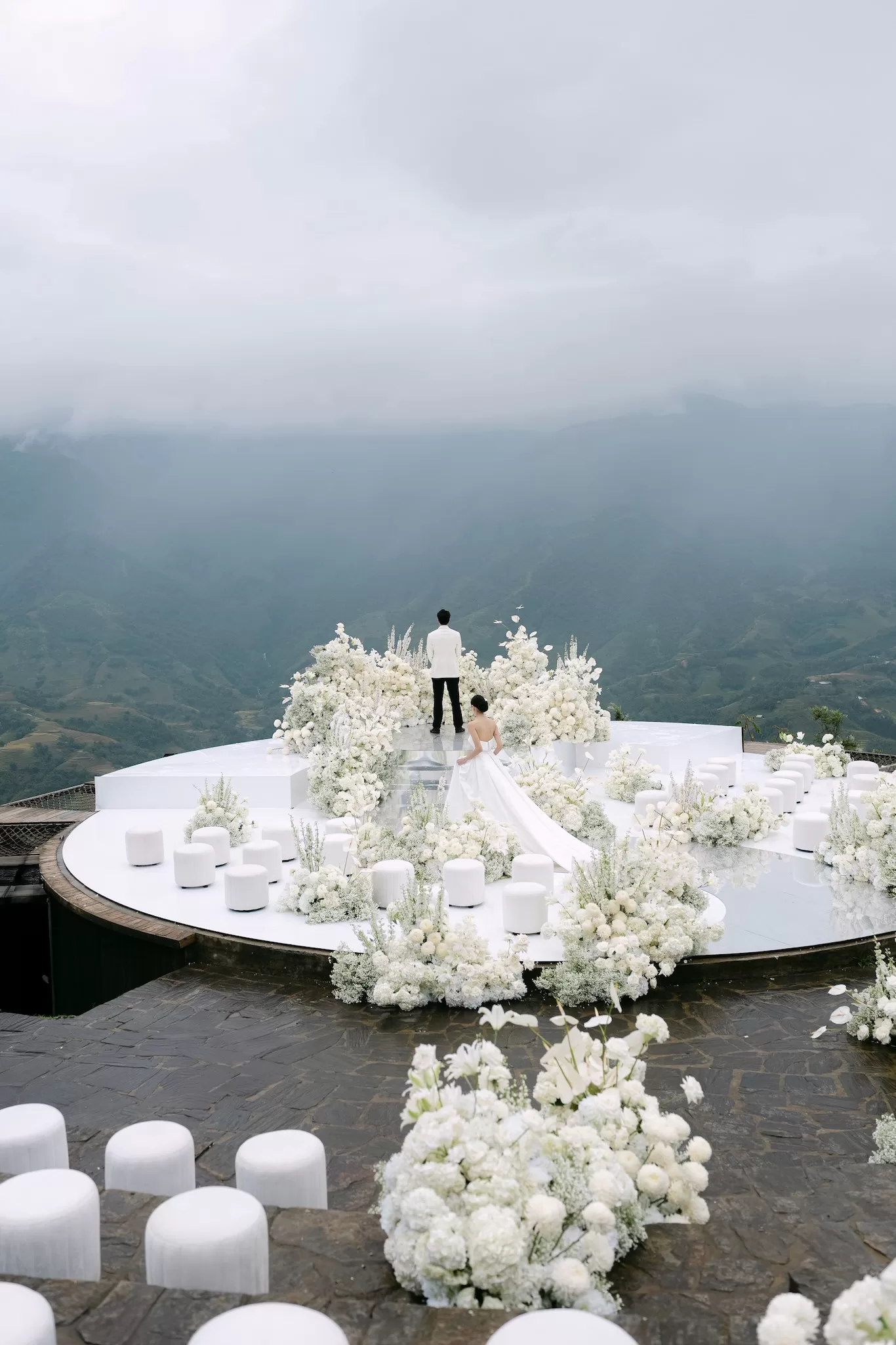 Bride walking toward groom on a reflective white ceremony platform framed by cascading florals and expansive mountain views at Ville de Mont Mountain Resort.