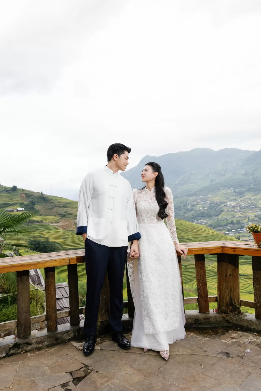 Bride and groom holding hands on a wooden balcony at Ville de Mont Mountain Resort with panoramic mountain landscape behind them.
