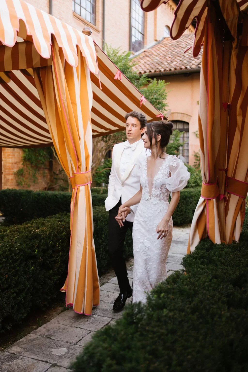 Bride and groom walking beneath elegant striped reception tents in a lush Italian garden during a wedding designed by Benevent Planner.