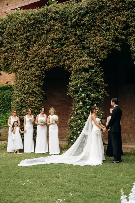 Ceremony scene with bridesmaids gathered beside ivy-covered archway at Castello di San Fabiano