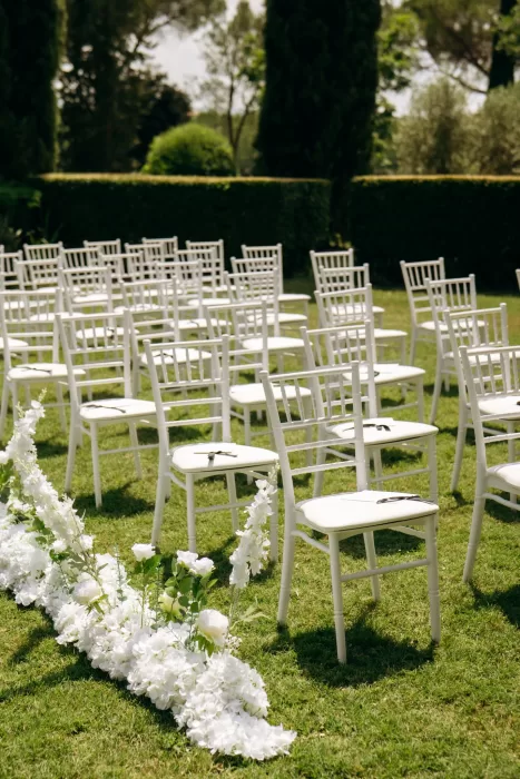 White ceremony chairs with floral aisle details on garden lawn at Castello di San Fabiano