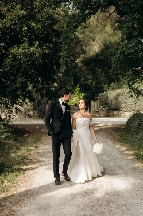 Bride and groom walking along shaded countryside path at Castello di San Fabiano, relaxed just-married moment