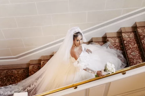 Bride with long veil and bouquet walking up an interior staircase at Château Bouffémont.