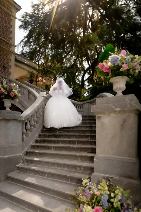 Bride descending the stone staircase with flowing veil and pastel floral arrangements at Château Bouffémont.