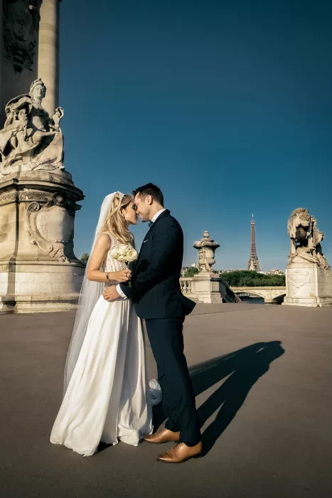 Bride and groom embracing on a Paris bridge with the Eiffel Tower visible in the background after their wedding at Château Bouffémont.