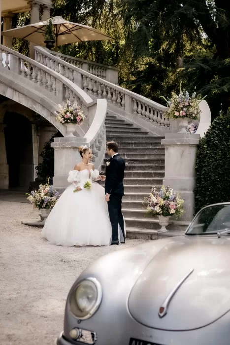 Bride and groom standing beneath the sweeping stone staircase adorned with pastel florals at Château Bouffémont.