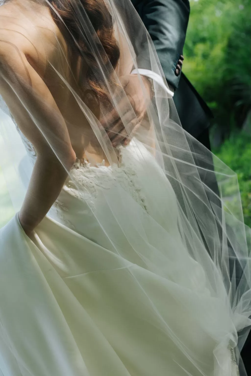 Close-up of the bride and groom in a gentle embrace, her veil softly catching the light in the Château Ste. Agnès garden.