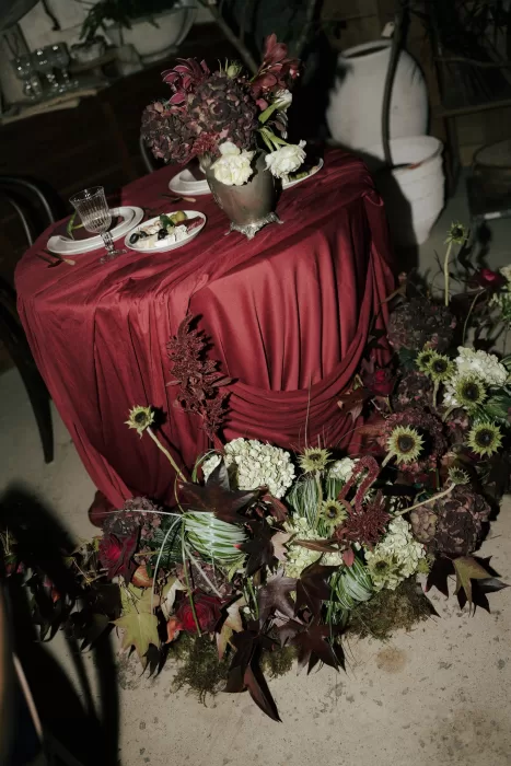 Burgundy reception table styling with dramatic floral arrangement and autumn-toned flowers at Common Goods.