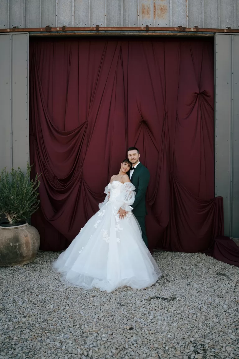 Bride and groom posing together in front of dramatic burgundy drapery at Common Goods wedding venue.