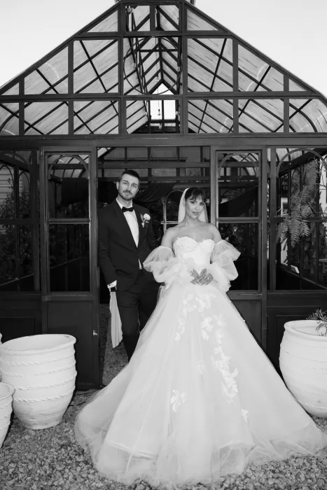 Newlyweds posing in front of the glass greenhouse structure at Common Goods, the bride wearing a dramatic tulle gown and veil.
