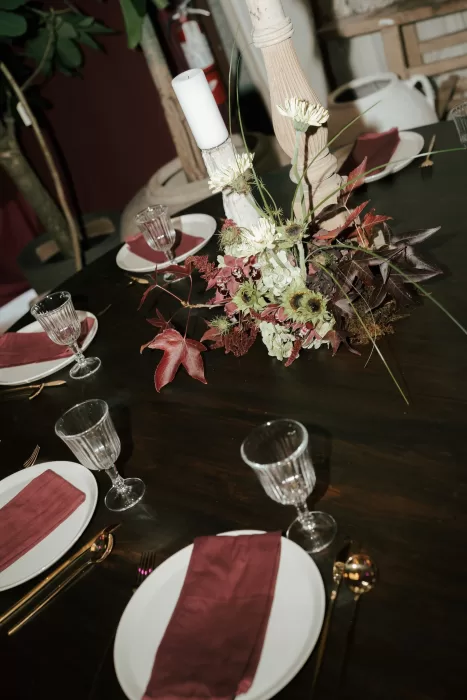 Reception table at Common Goods styled with burgundy napkins, gold flatware, and autumn-toned floral centerpiece.